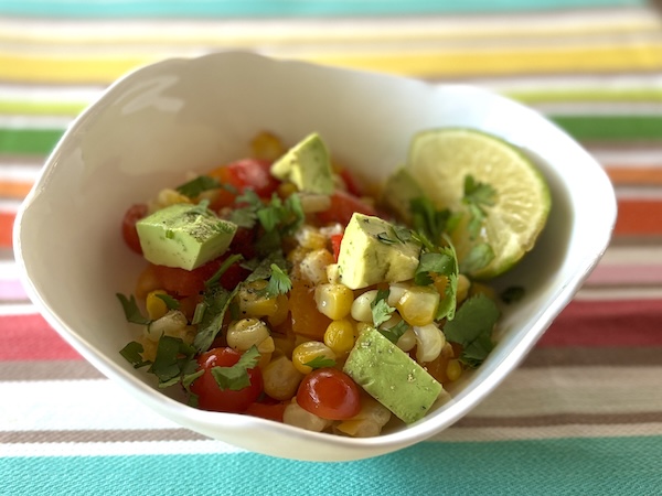 Bright summer corn salad in a white bowl on a colorful striped cloth